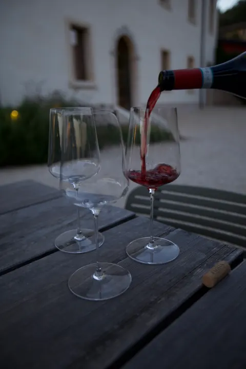 Il vino rosso versato in un calice su un tavolo di legno, all’aperto.